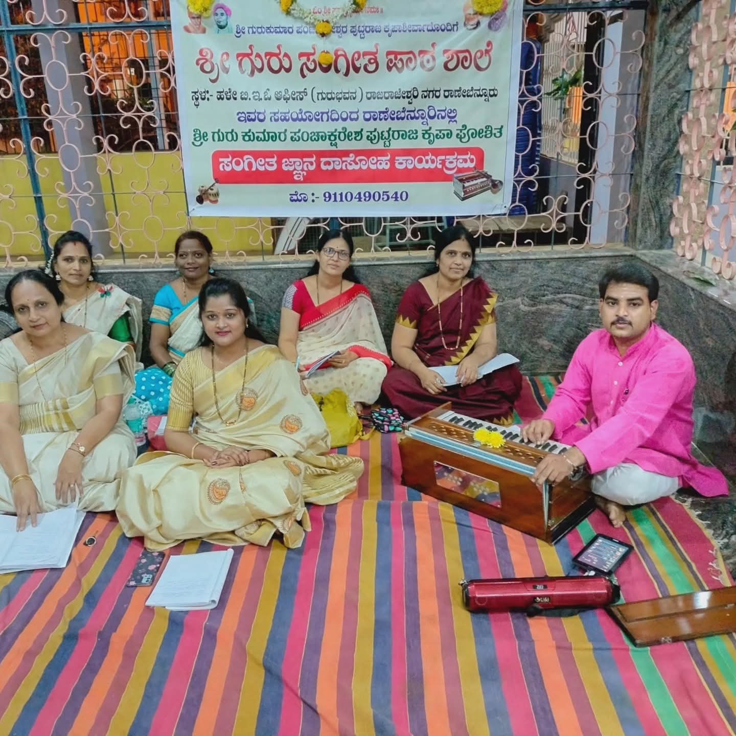 A group of students and teachers with a harmonium beneath the Vidyalaya banner
